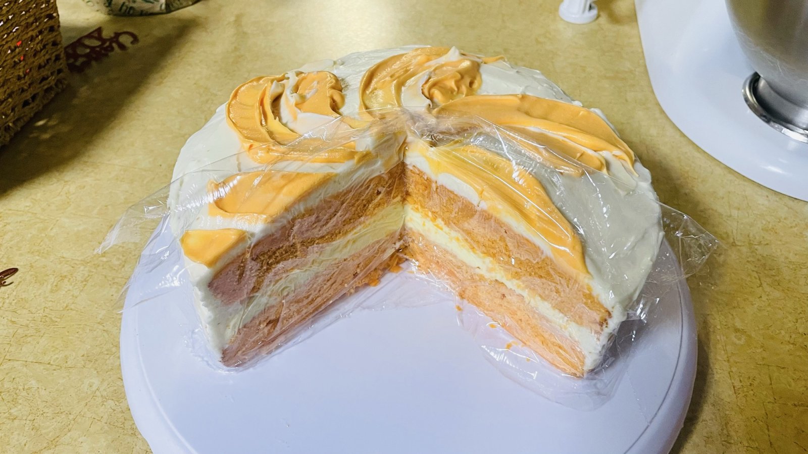 A home-made two-layer cake with orange cake, cream filling, and pale cream frosting, decorated with orange swirls on top