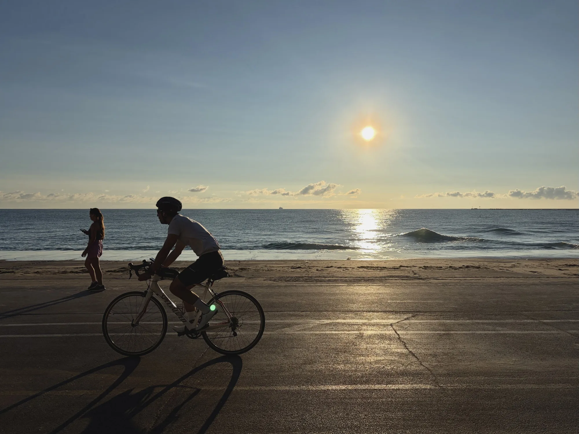 An image of the sun rising over the lakefront trail along Lake Michigan in Chicago. A biker and jogger are silhouette in the foreground&nbsp;by the sun.